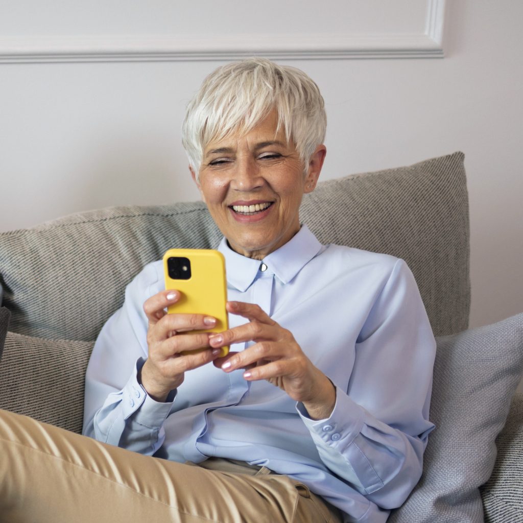 old lady sitting on a couch using her cell phone